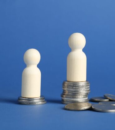 Financial inequality. Wooden figures with uneven amount of coins on blue background