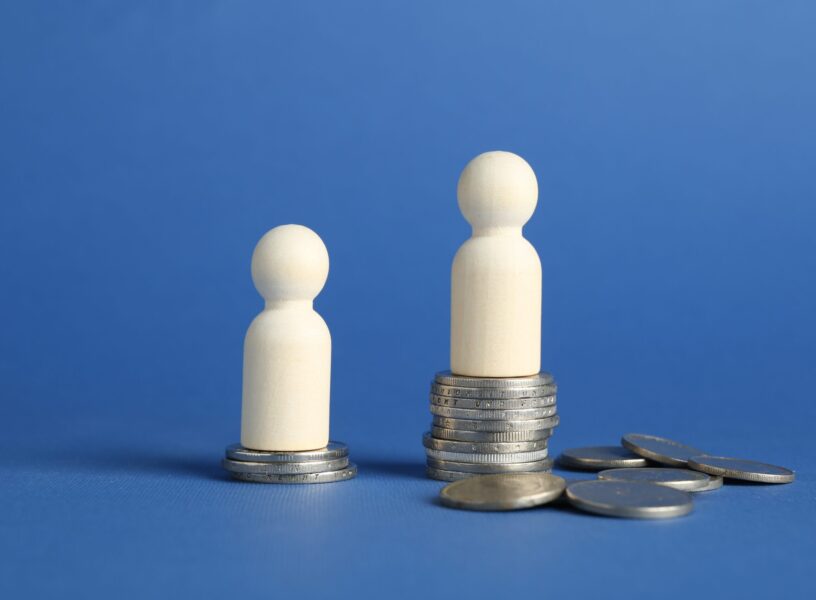 Financial inequality. Wooden figures with uneven amount of coins on blue background