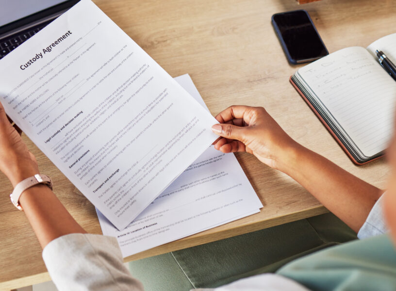 Family lawyer, hands and contract with attorney case and custody notes with agreement in a office. Desk, top view and law firm with planning and paperwork for report and document with child services
